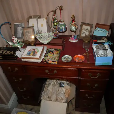 Sale Photo Thumbnail #46: Traditional wooden desk loaded with collectibles, framed vintage photos, decorative ornaments, small trinket boxes, and glassware.