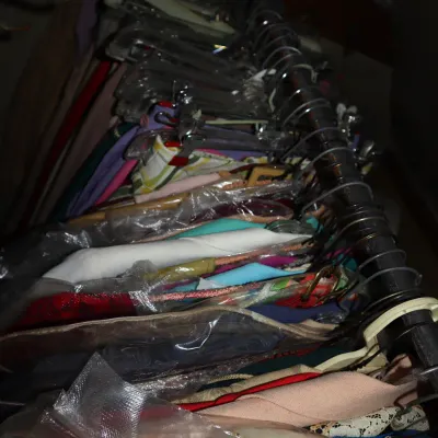 Sale Photo Thumbnail #24: Closet rack packed with various vintage garments on plastic and metal hangers, featuring colorful fabrics and protective plastic coverings.