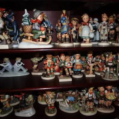 Sale Photo Thumbnail #4: Collection of vintage Hummel and Goebel porcelain figurines arranged on wooden display shelves.