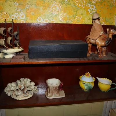 Sale Photo Thumbnail #135: Vintage dark wooden wall-hanging shelf displaying various decorative items, including a model sailing ship, a camel figure, a piece of coral, and ceramic pottery.