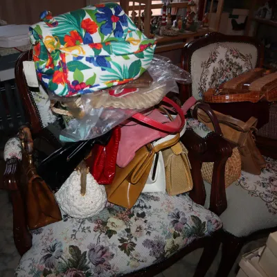 Sale Photo Thumbnail #53: Collection of vintage handbags and purses piled on top of two floral tapestry upholstered armchairs.