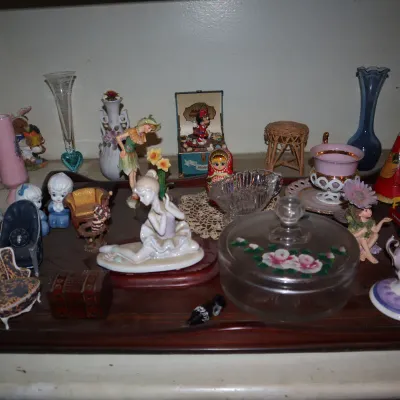 Sale Photo Thumbnail #114: Collection of vintage knick-knacks and collectibles, including porcelain figurines, glass vases, miniature furniture, and a floral trinket dish displayed on a wooden tray.