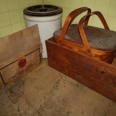Sale Photo Thumbnail #132: Vintage woven wooden picnic basket resting inside a stamped wooden crate, alongside a large stone crock with lid and an old Ball Mason jars cardboard box.
