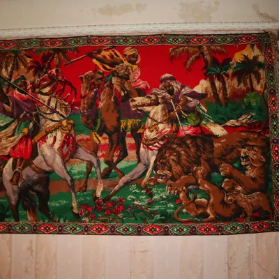 Sale Photo Thumbnail #110: Vintage Orientalist velvet wall tapestry depicting camel riders, horsemen, and lions with fringe trim hanging on a wall.