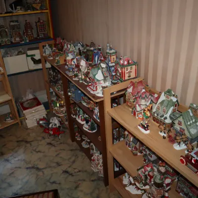 Sale Photo Thumbnail #36: Large collection of illuminated Christmas village buildings and accessories displayed on wooden shelving units.