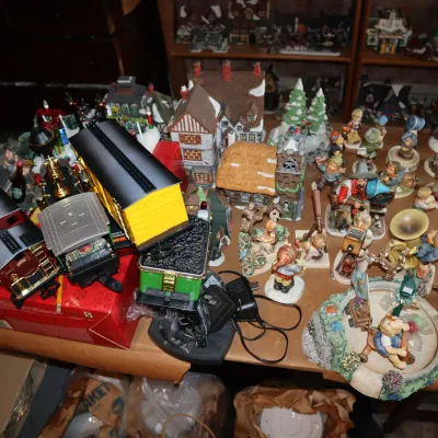 Sale Photo Thumbnail #27: Collection of holiday decorations featuring toy train cars, miniature Christmas village buildings, and various porcelain figurines.
