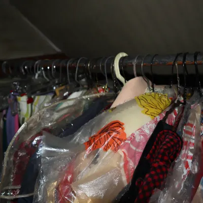 Sale Photo Thumbnail #25: Selection of vintage clothing and dresses hanging on a metal clothing rack, many stored in plastic garment bags.