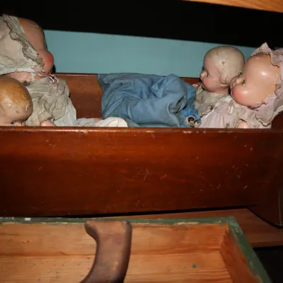 Sale Photo Thumbnail #73: Collection of vintage composite baby dolls in original bonnets and clothing, displayed inside a wooden toy cradle.