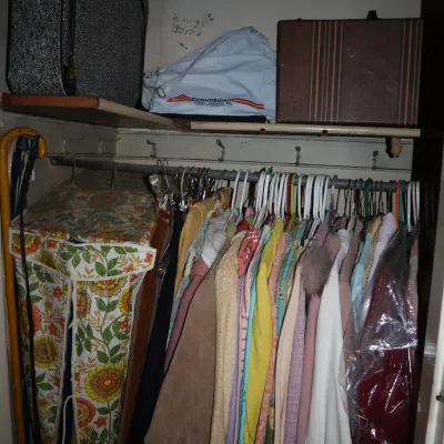 Sale Photo Thumbnail #155: Vintage clothing hanging in a closet alongside vintage suitcases and a vinyl garment bag featuring a 1970s floral pattern.