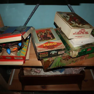 Sale Photo Thumbnail #71: Collection of vintage items on wooden shelving, including Tuco interlocking picture puzzles, O'Desco boxes, and a boxed vintage Christmas light set.