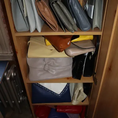 Sale Photo Thumbnail #17: Collection of vintage leather and vinyl clutch purses and handbags organized on wooden cabinet shelves in a variety of colors.