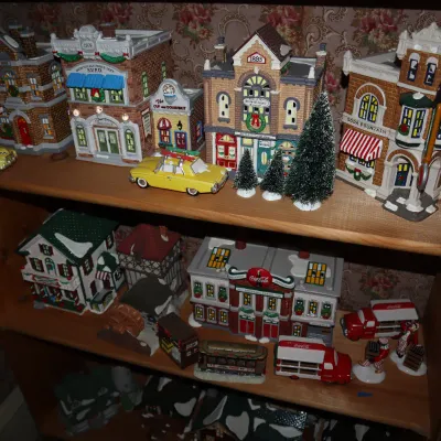 Sale Photo Thumbnail #14: Collection of Department 56 Snow Village buildings and Coca-Cola collectibles, displayed on wooden shelving.