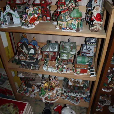Sale Photo Thumbnail #39: Collection of Christmas village miniature buildings, Santa figurines, and holiday decorations arranged on a wooden shelving unit.