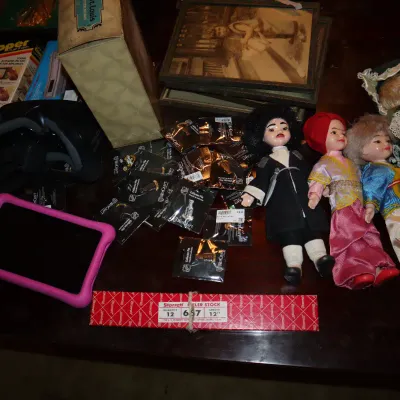 Sale Photo Thumbnail #120: Eclectic assortment of items including vintage collectible dolls, packaged lapel pins, a VR headset, Starrett feeler stock, tablet devices, and framed artwork.