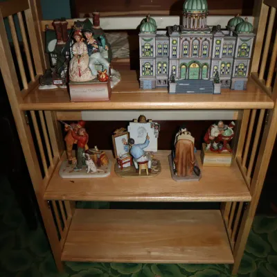 Sale Photo Thumbnail #58: Collection of Norman Rockwell figurines and decorative village buildings displayed on a three-tier light oak folding bookshelf.