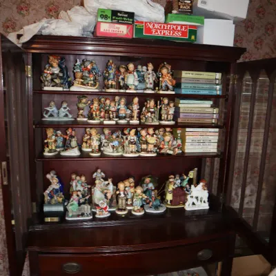 Sale Photo Thumbnail #3: Vintage dark wood curio cabinet filled with a large collection of Goebel Hummel porcelain figurines and hardcover books.