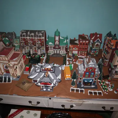 Sale Photo Thumbnail #63: Large collection of illuminated Christmas village buildings, figurines, and accessories displayed on a tabletop.
