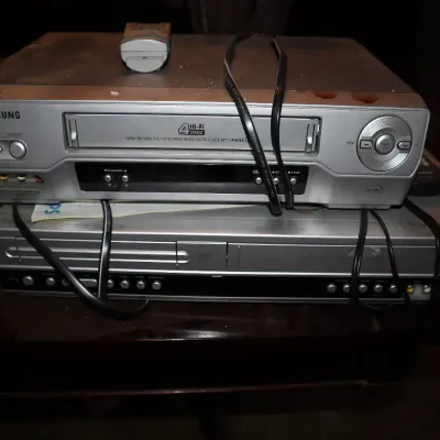 Sale Photo Thumbnail #124: Samsung silver VCR player stacked on top of a DVD player component, complete with power cords and remotes.