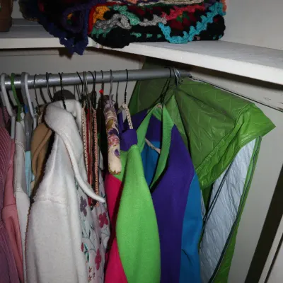 Sale Photo Thumbnail #153: Selection of vintage clothing and a vibrant crochet afghan blanket stored on a closet shelf.