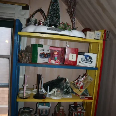 Sale Photo Thumbnail #40: Primary-colored wooden shelving unit displaying a collection of vintage holiday decorations, boxed figurines, and porcelain village buildings.