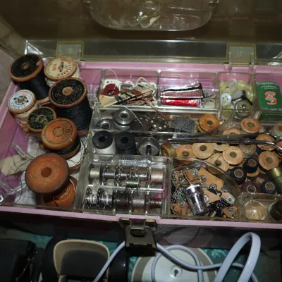 Sale Photo Thumbnail #97: Vintage pink plastic sewing caddy filled with various sewing notions, including wooden spools of thread, metal bobbins, thimbles, and scissors.