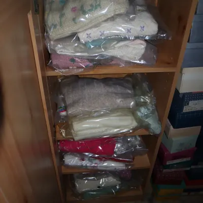Sale Photo Thumbnail #31: Light wood storage cabinet filled with plastic-wrapped folded knit sweaters and textiles on its shelves.