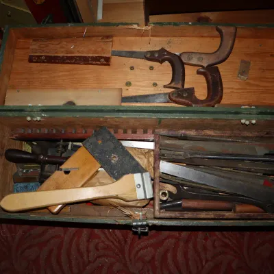 Sale Photo Thumbnail #68: Vintage painted green wooden carpenter's chest filled with various hand tools, including handsaws, metal files, a wooden square, and scraper.