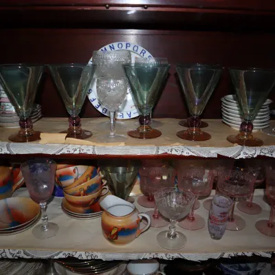 Sale Photo Thumbnail #128: Collection of vintage glassware and china inside a hutch, including iridescent green stemware, pink depression glass goblets, and hand-painted tea service pieces.