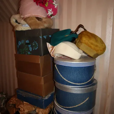 Sale Photo Thumbnail #34: Collection of vintage women's hats, including floral-trimmed, faux fur, and pillbox styles, displayed atop stacks of hat and shoe boxes.