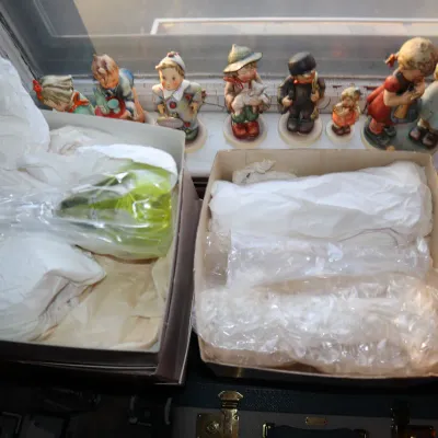Sale Photo Thumbnail #16: Collection of vintage Goebel Hummel porcelain figurines displayed on a windowsill behind boxes containing wrapped glassware.