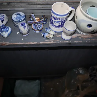 Sale Photo Thumbnail #175: Collection of blue and white Delftware-style souvenirs and trinkets displayed on a windowsill, including a Cape Cod stein, miniature wooden shoes, windmills, and heart-shaped boxes.