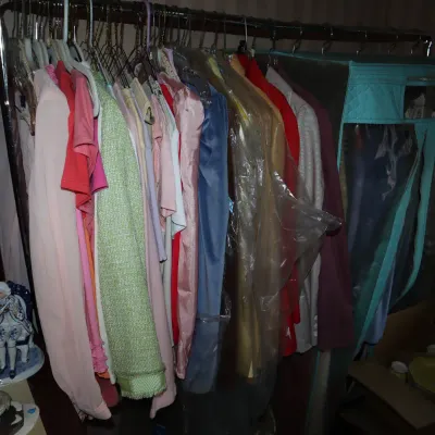 Sale Photo Thumbnail #50: Metal rolling garment rack filled with vintage women's clothing, including dresses, jackets, and blouses, alongside a teal portable wardrobe closet.