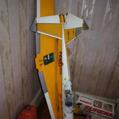 Sale Photo Thumbnail #89: Large yellow and white RC model airplane fuselage with Pennzoil decals, standing upright against a wall alongside a Eureka Enviro Steamer box.