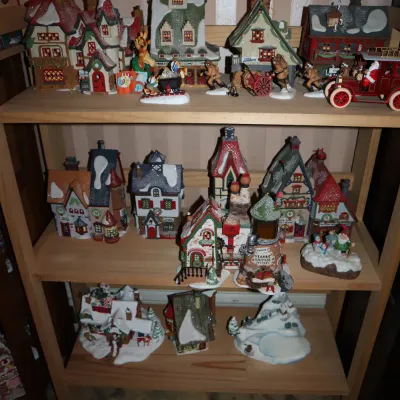 Sale Photo Thumbnail #37: Collection of Dept 56 and similar ceramic Christmas village houses and figurines displayed on light wood shelving.