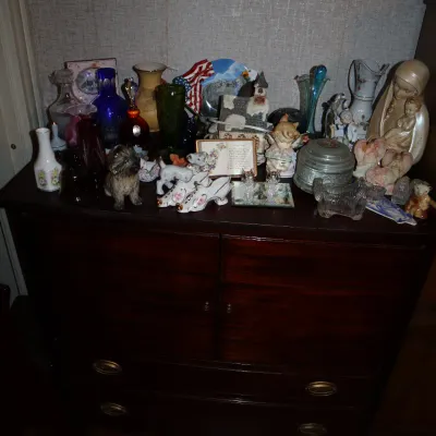 Sale Photo Thumbnail #149: Dark wood chest of drawers topped with a large collection of vintage knick-knacks, glassware, porcelain figurines, and decorative porcelain shoes.
