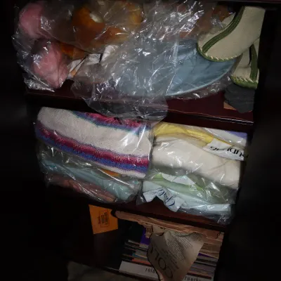 Sale Photo Thumbnail #35: Dark wooden shelf unit filled with plastic-wrapped textiles, clothing, a hat, shoes, and vintage paper ephemera.