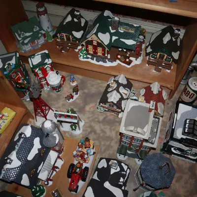 Sale Photo Thumbnail #15: Large collection of illuminated Christmas village ceramic houses, figurines, and accessories displayed on wooden shelves and the floor.