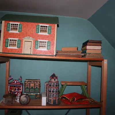 Sale Photo Thumbnail #69: Vintage Rich Toys wooden dollhouse with red brick finish and green shutters, displayed on shelving alongside books and various miniature buildings.