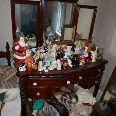 Sale Photo Thumbnail #162: Dark wood vanity table with a tri-fold mirror, filled with various vintage collectibles including a Santa figurine, small glass vases, and porcelain trinkets.