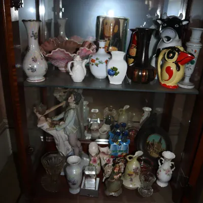 Sale Photo Thumbnail #119: Collection of decorative porcelain, glass figurines, and small vases displayed on glass shelves inside a wooden curio cabinet.