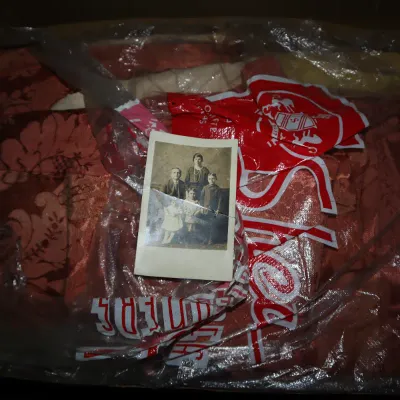 Sale Photo Thumbnail #61: Vintage black-and-white family portrait resting on a plastic-wrapped reddish damask textile in a storage box.