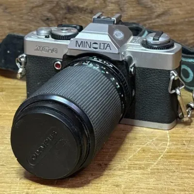 Sale Photo Thumbnail #567: Lot 671: Vintage Minolta XG-A 35mm SLR film camera with a manual focus zoom lens
