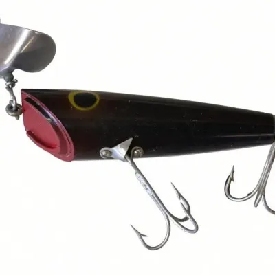 Sale Photo Thumbnail #122: Lot 195: Vintage hard-plastic fishing lure. Black tapered body with red top section, yellow eye ring, metal spinner blade, two treble hooks, and a cork/wood tail piece. Shows light wear. Classic mid-century spinner style