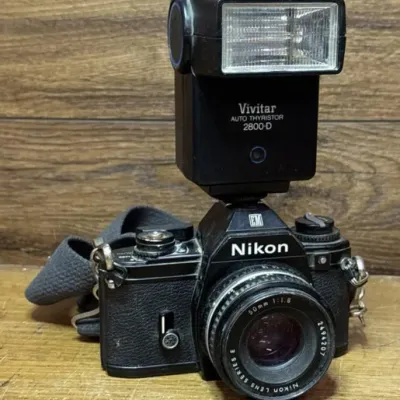 Sale Photo Thumbnail #568: Lot 672: Vintage Nikon EM 35mm film SLR camera equipped with a 50mm lens and a mounted Vivitar shoe-mount flash