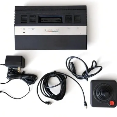 Sale Photo Thumbnail #3: Lot 4: 1970s Atari 2600 Console Bundle – Power Adapter, RF Cables & Original Joystick - power light comes on - Vintage Atari 2600 (Video Computer System) console, the iconic home video game system from the late 1970s–early 1980s. Black plastic case wi