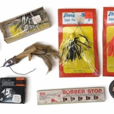 Sale Photo Thumbnail #106: Lot 179: Vintage fishing tackle lot. Includes a metal spinning reel crank/handle with beige knob, black Zebco extra-spools box (model 33-44), a feathered metal-head lure, packaged Hawaiian Wiggler-style lure, a package of Bobber Stop floats, two Finny Sup