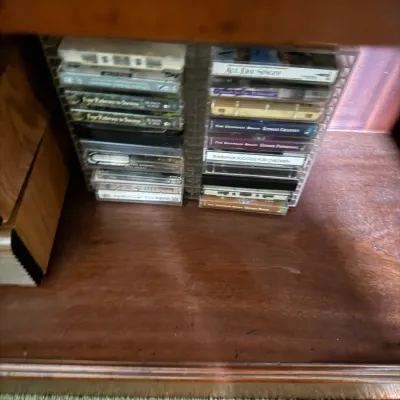 Sale Photo Thumbnail #114: Collection of audio cassette tapes stored in a plastic rack inside a wooden cabinet.