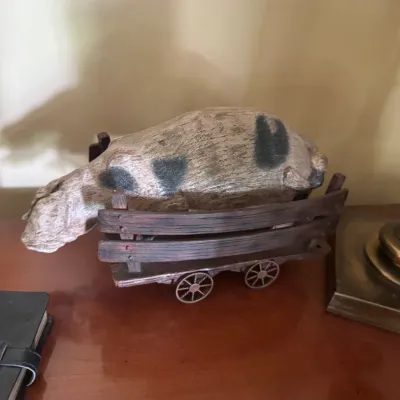 Sale Photo Thumbnail #48: Rustic carved resin figurine of a spotted pig resting inside a wooden farm wagon.