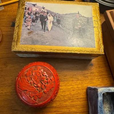 Sale Photo Thumbnail #171: Vintage rectangular gold-embossed trinket box with a Scottish wedding print lid alongside a small round carved red cinnabar lacquer box.
