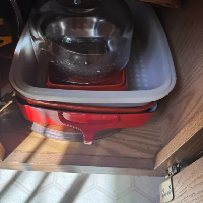 Sale Photo Thumbnail #227: Stack of vintage kitchenware stored inside a wooden cabinet, including a red cast iron roasting pan, a plastic basin, and a clear glass cake dome.